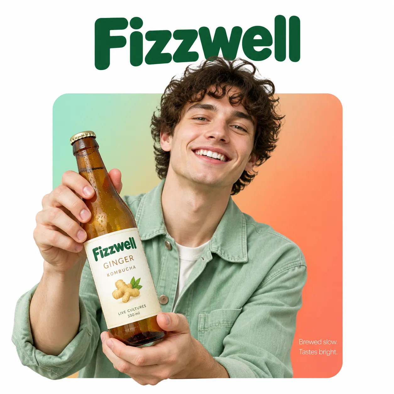 Grinning curly-haired man holding a Fizzwell ginger kombucha bottle, breaking out of a mint-to-coral gradient rounded square, green brand name above